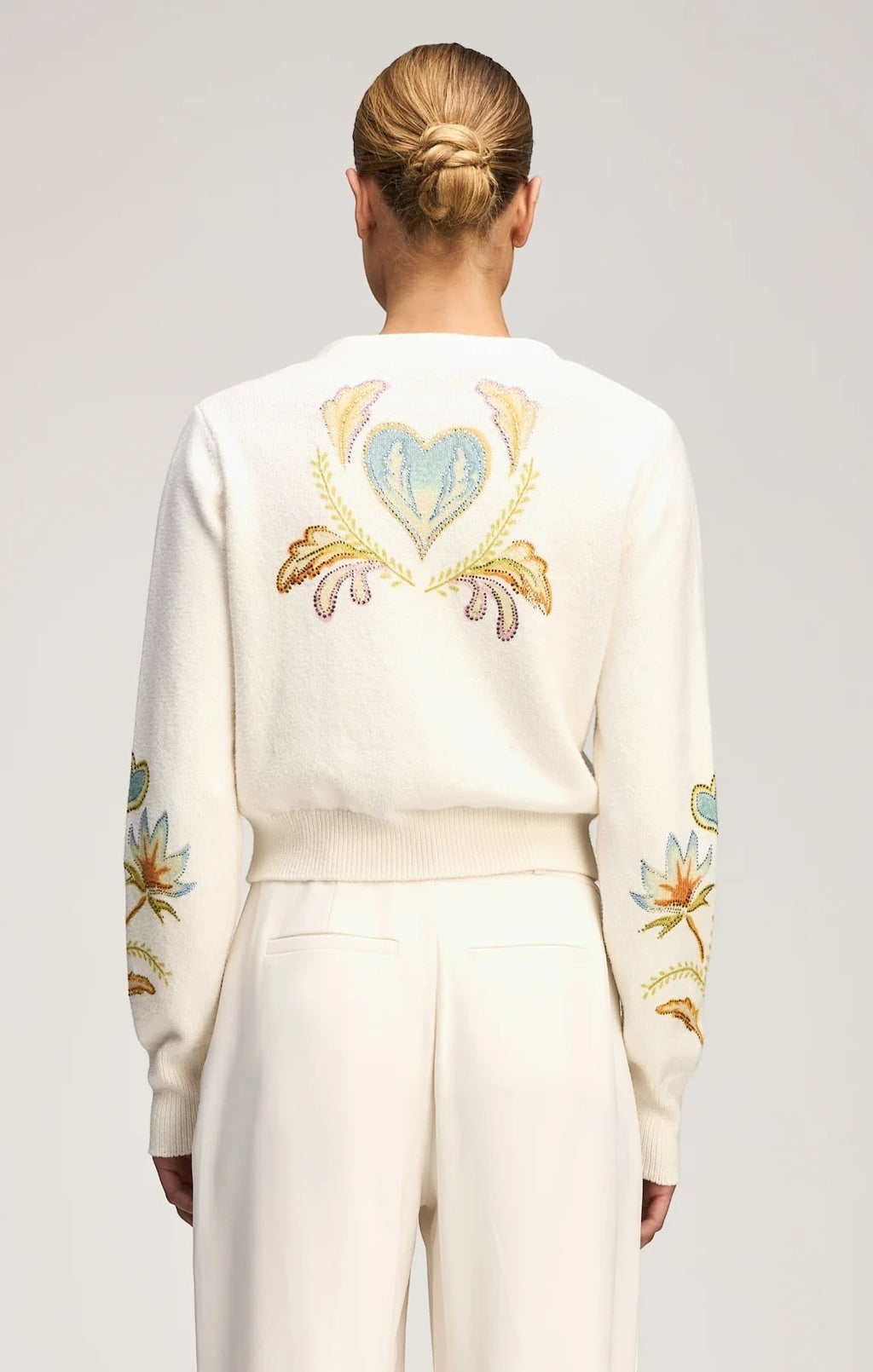Back view of a Coats and co. cream knit cardigan featuring vibrant floral and heart embroidery on the back and sleeves