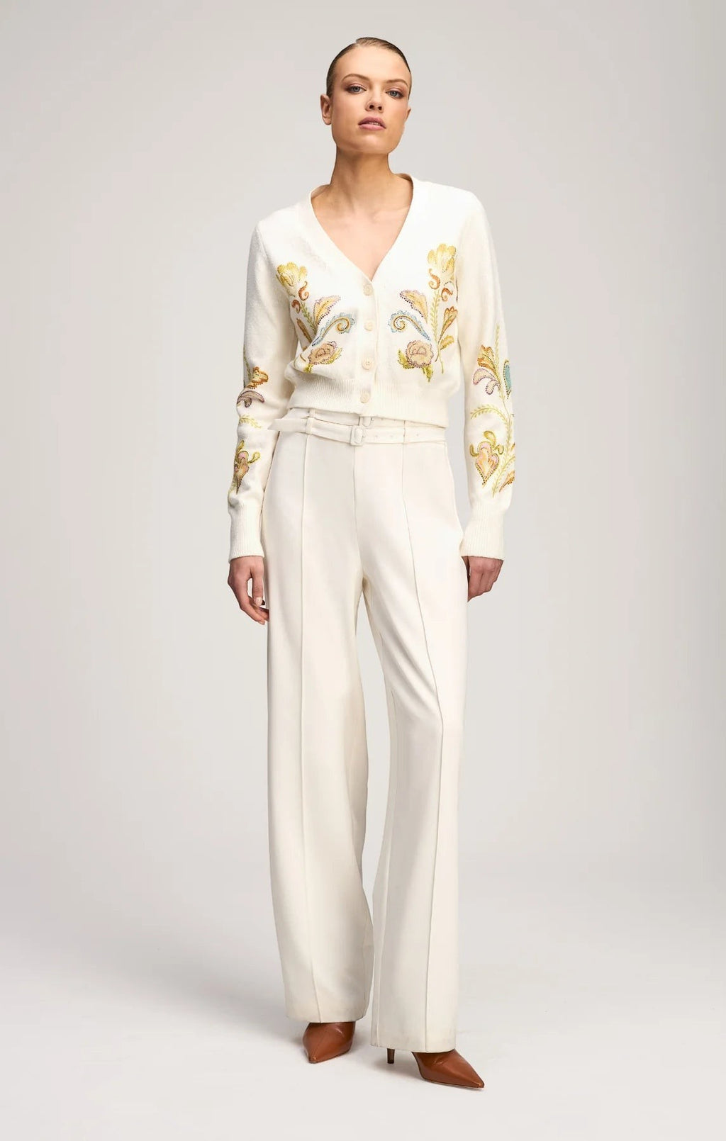 Model wearing a Coats and co. cream V-neck cardigan with intricate floral embroidery, paired with white wide-leg trousers.